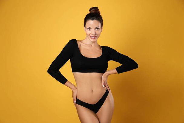 Beautiful woman in black sexy panties on yellow background - Foto, afbeelding