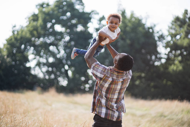 African father throwing up son in air on summer field - Фото, изображение