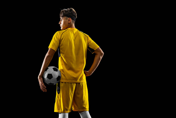 Gesneden portret van jonge professionele voetballer geïsoleerd over zwarte achtergrond. Achteraanzicht - Foto, afbeelding