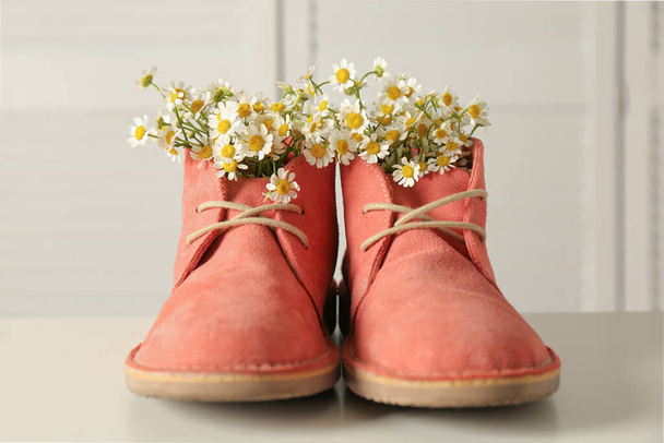 Beautiful tender chamomile flowers in pink boots on white table - Foto, Imagem