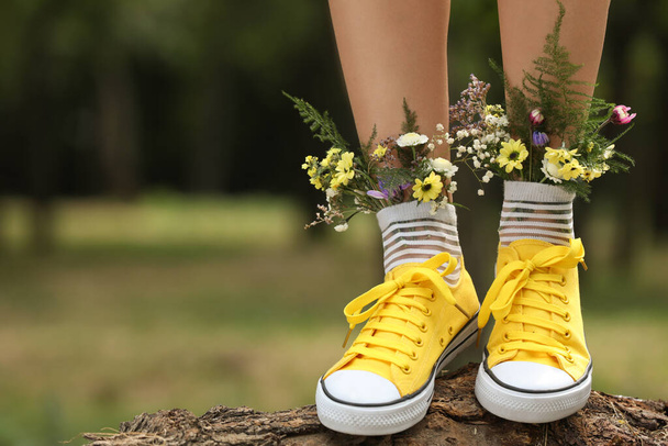 Woman standing on log with flowers in socks outdoors, closeup. Space for text - Foto, Bild