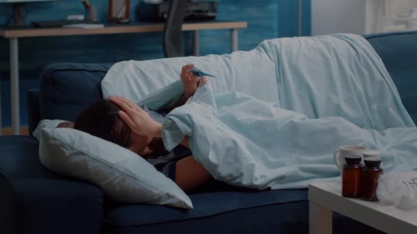 Osoba chora leżąca na kanapie i trzymająca termometr - Materiał filmowy, wideo