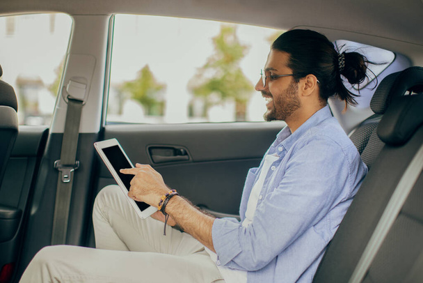 Arab guy in casual outfit sitting at taxi, using pad - Photo, Image