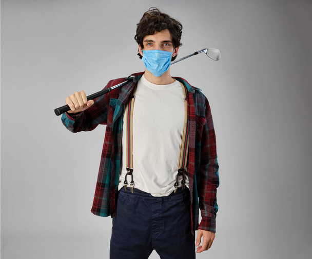 Гольф в повседневной одежде и в защитной маске ковид-19, он держит утюг для гольфа. - Фото, изображение