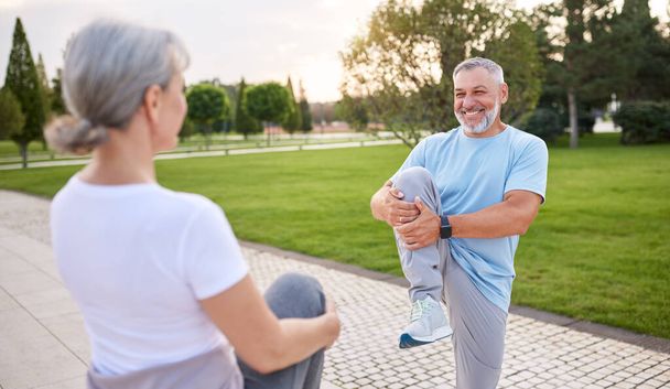 Glückliche ältere Familien, die gemeinsam draußen Sport treiben, gesunde Senioren, die gemeinsam im Stadtpark Dehnübungen machen, positive Rentner, die sich im Freien sportlich betätigen - Foto, Bild