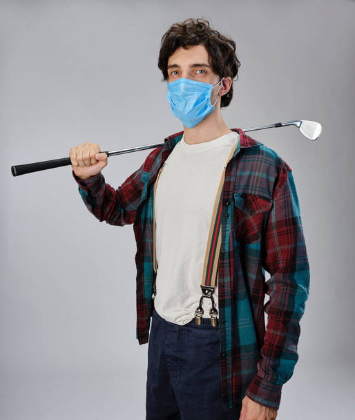 Golfista em roupas casuais e com uma máscara protetora covid-19, ele está segurando um ferro de golfe. - Foto, Imagem