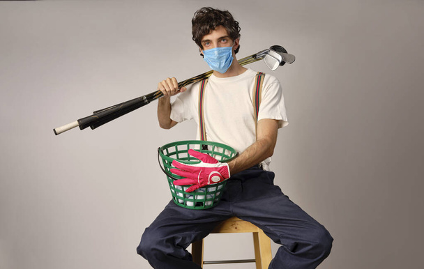 保護のcovid-19マスクを身に着けているカジュアル衣類のゴルフプレーヤー,いくつかのゴルフアイアンとゴルフドライブを保持します。 - 写真・画像