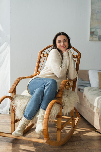 vue pleine longueur de la femme en pull chaud et chaussettes souriant à la caméra dans un fauteuil à bascule - Photo, image