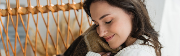 pleased woman with closed eyes holding soft blanket near face, banner - Photo, Image