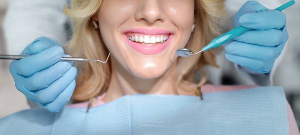 Κλείσιμο γυναικείου χαμόγελου και χεριών οδοντιάτρου με εργαλεία - Φωτογραφία, εικόνα