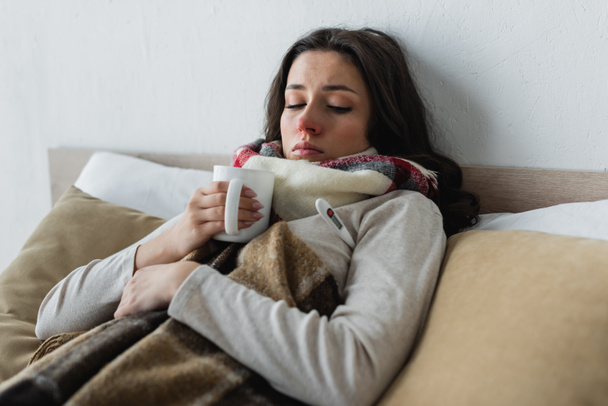 donna malata sdraiata sotto coperta a scacchi con tazza di tè - Foto, immagini