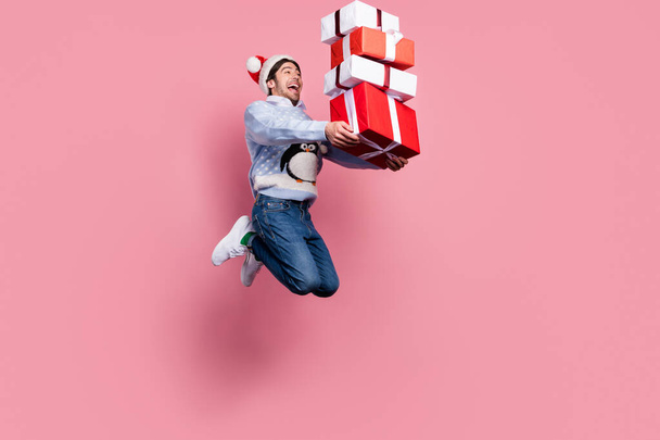 Photo of impressed cute man dressed blue christmas pullover jumping holding presents pile smiling isolated pink color background - Valokuva, kuva