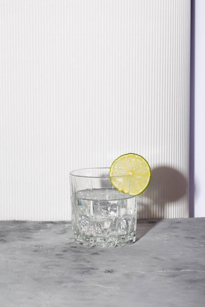 Vodka with ice and lime in glass on white background. Shadows and sunlight trendy - Fotó, kép