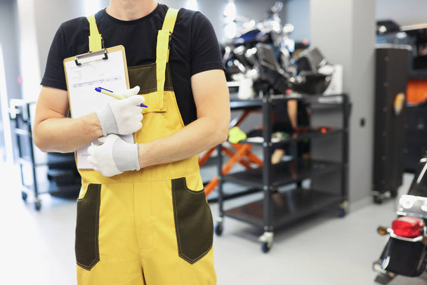 Auto monteur slotenmaker in geel uniform staat in auto reparatiewerkplaats closeup - Foto, afbeelding