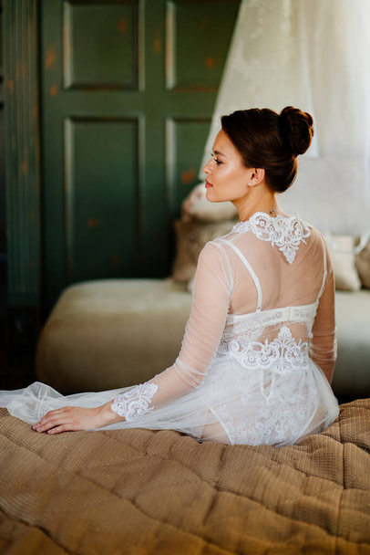 view from back. bride in lace robe sitting in bed. morning before the wedding. - Φωτογραφία, εικόνα