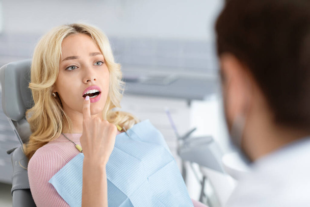 Приваблива блондинка відвідує стоматологічну клініку, вказуючи на зуб
 - Фото, зображення
