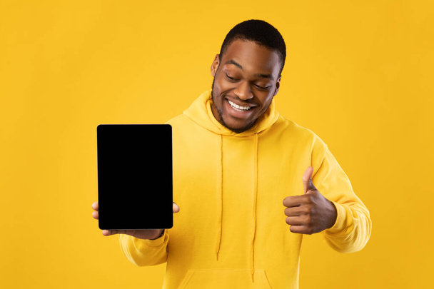 Afrikaanse man toont tablet scherm Gesturing duimen-Up over gele achtergrond - Foto, afbeelding