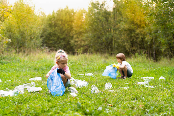 les enfants retirent les déchets en plastique et les mettent dans un sac à ordures biodégradable à l'air libre. Le concept d'écologie, de traitement des déchets et de protection de la nature. Protection de l'environnement. - Photo, image
