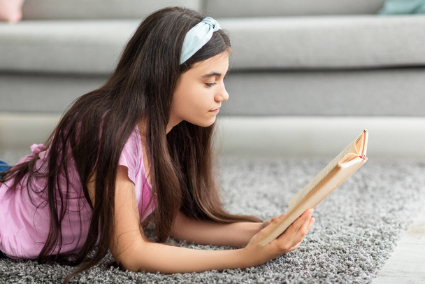家庭の娯楽の概念を維持する。インテリジェントインドのティーン女の子読書興味深い本,リビングルームの床に横たわって - 写真・画像