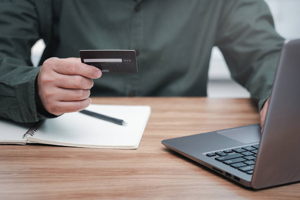 Biznesmen posiadają kartę kredytową w ręku do dokonywania bankowości internetowej, dokonywania płatności lub zakupu w Internecie i laptopa komputera na stole - Zdjęcie, obraz