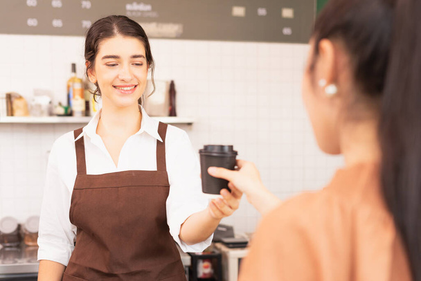 美しい白人バリスタの女性は、お客様にテイクアウトのコーヒーカップを提供し、コーヒーカップを受けながらコーヒーカップを見て喜んでいます。コーヒーバーとフードサービスビジネスでバリスタの仕事 - 写真・画像