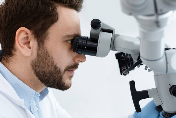 Stomatolog z brodą patrzący na mikroskop dentystyczny - Zdjęcie, obraz