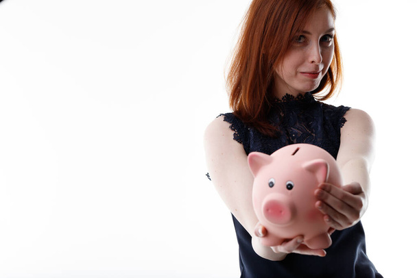 Mladá žena držící prasečí banku nataženou ke kameře s úsměvem spokojenosti ve spořicím a investičním či finančním konceptu - Fotografie, Obrázek