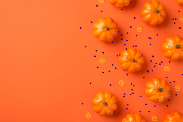 Top view photo of halloween decorations small pumpkins silhouettes and violet sequins on isolated orange background with copyspace - Foto, imagen