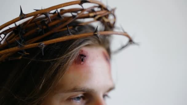 Jesús en una corona de espinas con heridas en la cara sobre un fondo blanco. De cerca. - Metraje, vídeo