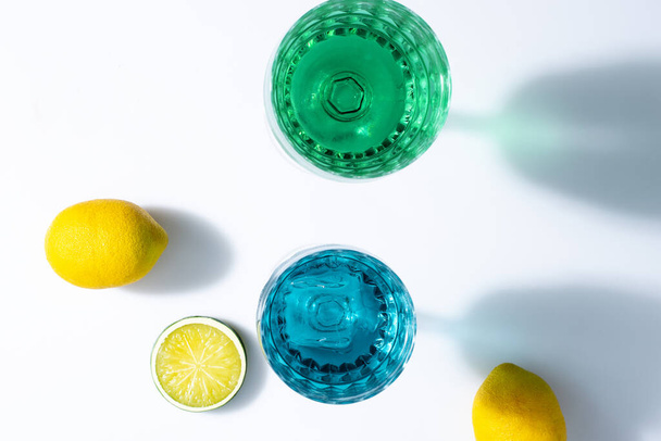 A top view of blue and green glasses with lemons on the white table - 写真・画像