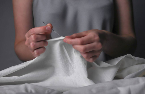 Manual sewing with needle in hands. Woman stitching on pastel cloth - Foto, afbeelding