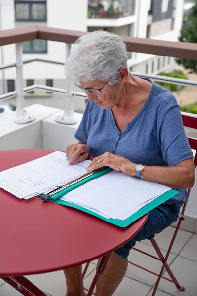 An elderly woman reads written administrative documents sitting at a table - Photo, Image