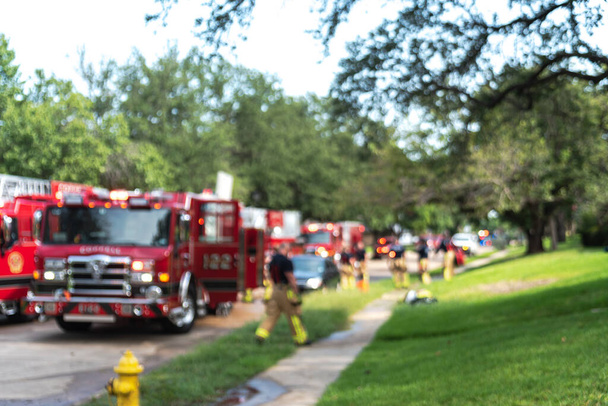 Пожарный размыл движение, гуляя по улице и по тротуару жилого дома в пригороде Далласа, штат Техас, Америка. Ряд пожарной машины с лестницами и работающими пожарными для страхования от пожара - Фото, изображение