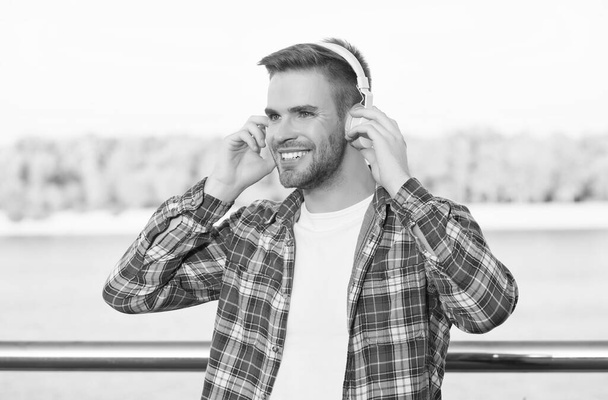 smiling bearded man listen music in digital earphones wearing checkered shirt outdoor, technology - Foto, Bild