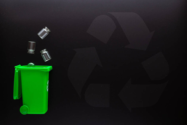 Trash glass recycle. Bin container for disposal garbage waste and save environment. Green dustbin for recycle glass can trash on black background. Top view - 写真・画像