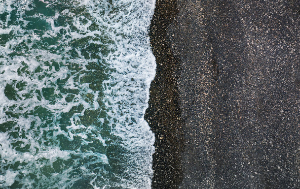 Mořské vlny lámání na divoké pláži s černým pískem a oblázky, letecké přírodní pozadí - Fotografie, Obrázek