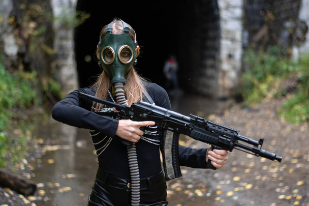 een vrouw in een zwart pak en gasmasker met een machinegeweer in haar handen - Foto, afbeelding