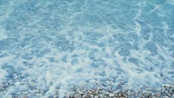 Golven spetteren op een kust vol kiezelstenen. Helder water bij de kust met kiezelstenen aan de onderkant. - Video