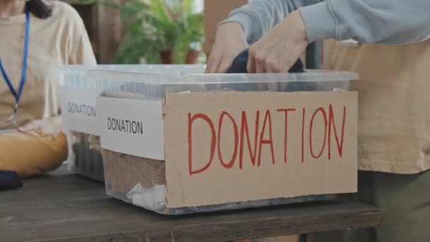Lento primer plano de manos masculinas irreconocibles de voluntarios poniendo ropa donada en recipientes de plástico antes de dárselos a la caridad - Imágenes, Vídeo