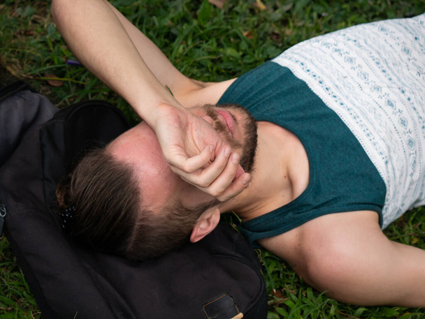 Bílý muž leží na trávě a zakrývá si tvář paží. - Fotografie, Obrázek