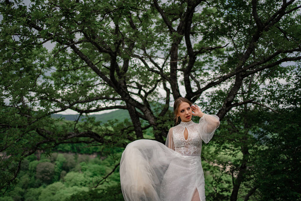 A bride in a white dress stands in the mountain forest - 写真・画像