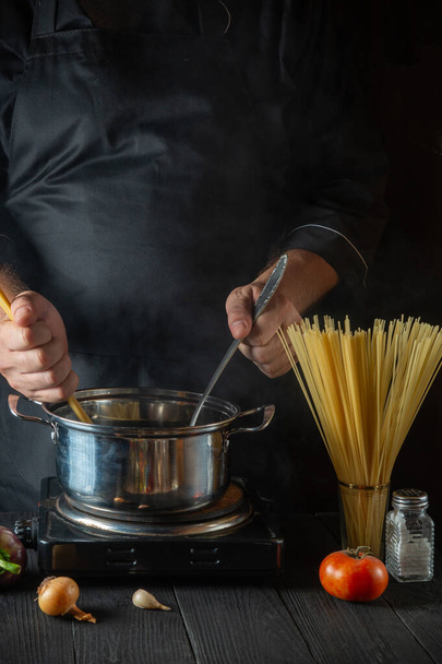 Chef bereidt Italiaanse pasta in een pan met groenten. Close-up van kok handen tijdens het koken in restaurant keuken. - Foto, afbeelding