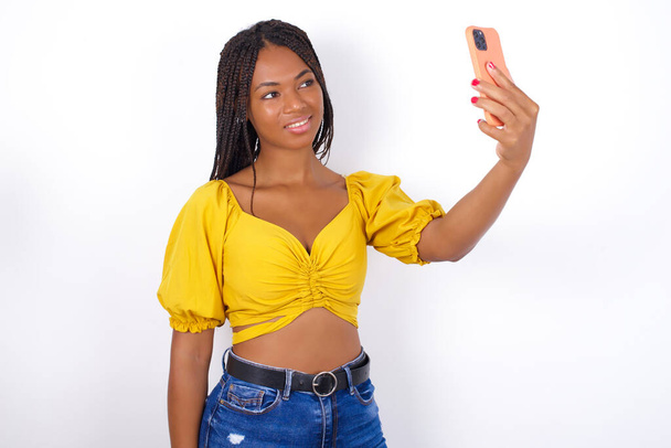 Porträt einer jungen schönen Frau mit gelbem Oberteil und Jeans, die ein Selfie macht, um es Freunden und Followern zu schicken oder es in seinen sozialen Medien zu posten. - Foto, Bild