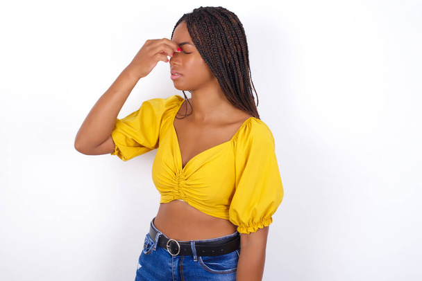 Triste joven hermosa mujer usando top amarillento y jeans que sufren de dolor de cabeza sosteniendo la mano en su cara - Foto, imagen