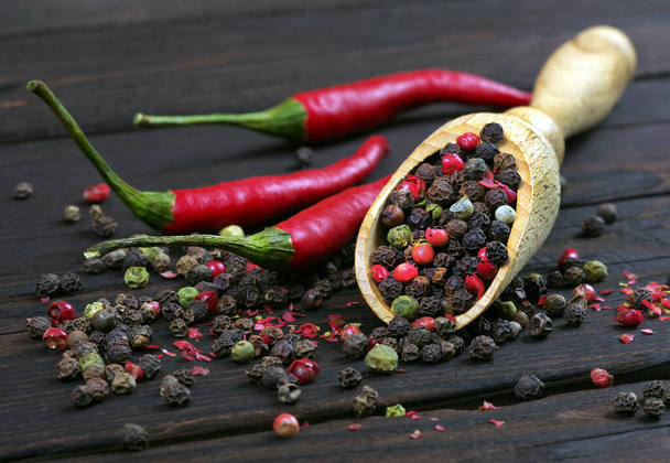 rode hete chili pepers en een mengsel van pepers in een houten lepel op een houten tafel. peper mengsel. traditionele specerijen. - Foto, afbeelding