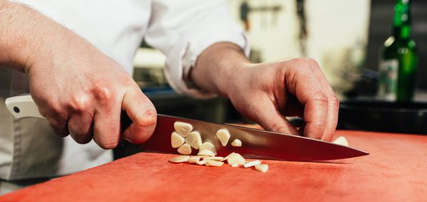 Mannelijke chef-kok snijdt knoflook tijdens het bereiden van een maaltijd in de keuken van een restaurant. - Foto, afbeelding