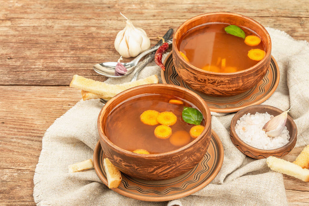 Transparent chicken broth with vegetables in ceramic bowls. Traditional bouillon, healthy food, cutlery. Old wooden background, copy space - Photo, Image