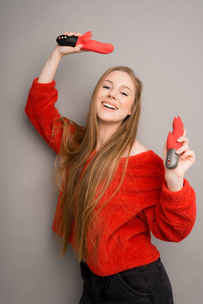 Sex toys in the hands of an attractive long-haired girl.Red dildo and dildo.Useful for sex shops - Φωτογραφία, εικόνα