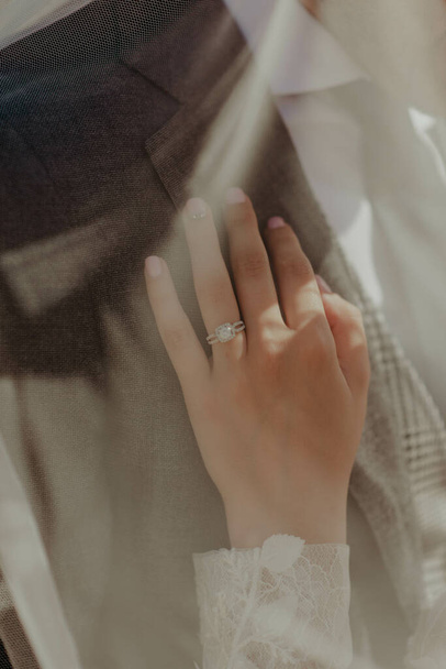 A bride's hand with engagement ring on her finger touching her groom's garment - Foto, Imagem