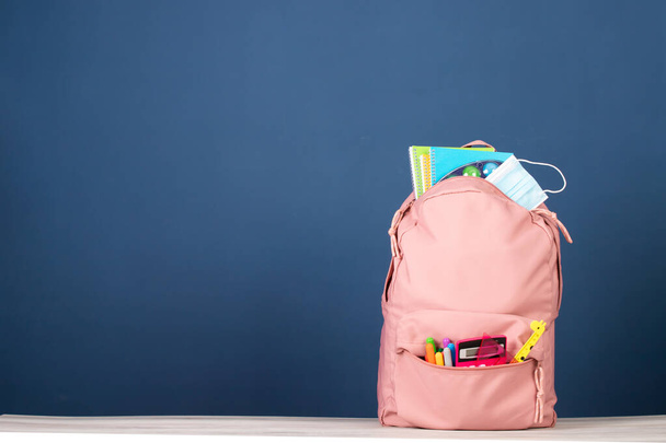 Backpack with school supplies and medical mask. COVID-19 prevention while going back to school and new normal concept. - Photo, Image